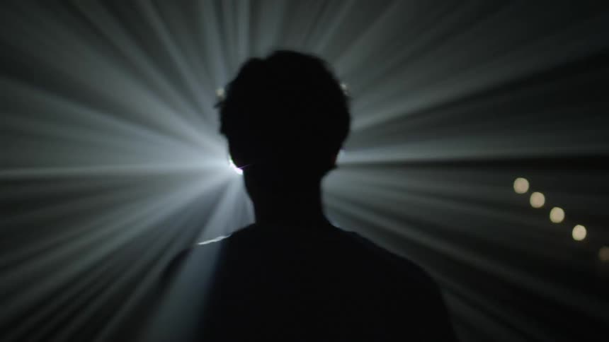 A young man walking away from a strobe light and then turning back to walk towards it