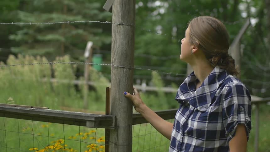 A woman gazes out into the woods beyond the fence