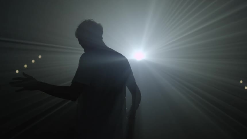 A shadowed view of a man dancing with a bright light behind him