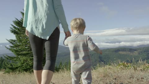 Woman and baby walk through dry grass