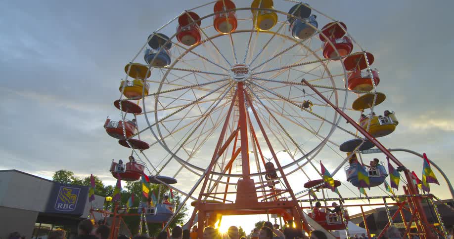 A ferris wheel rotates while a crowd passes by