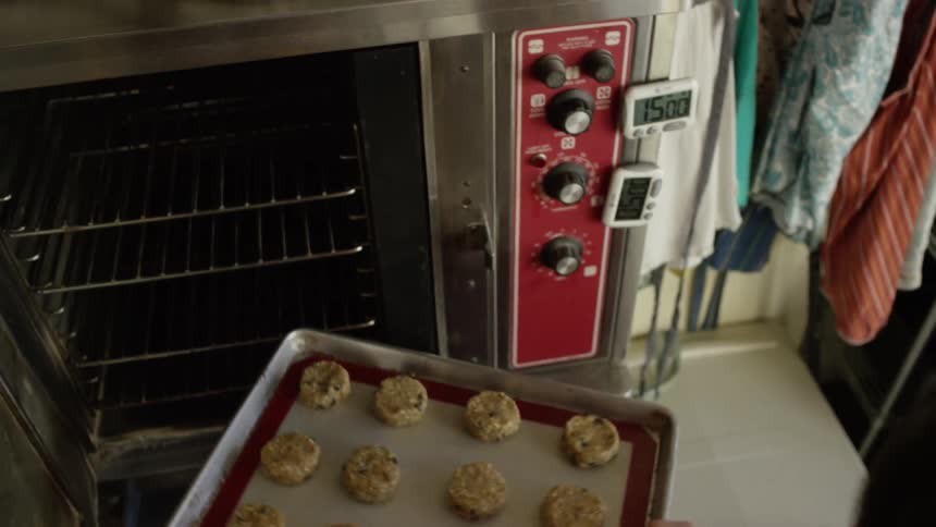 A woman places a baking pan full of cookies into an industrial oven
