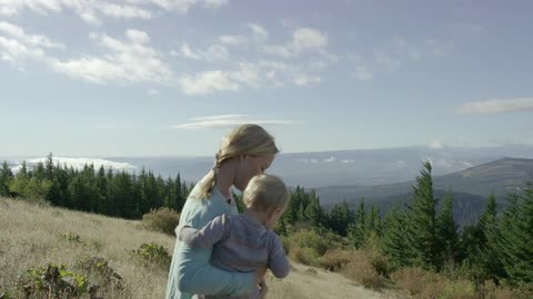 Woman carrying child and putting it down on a grassy hill