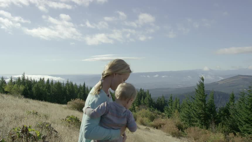 Woman carrying child and putting it down on a grassy hill