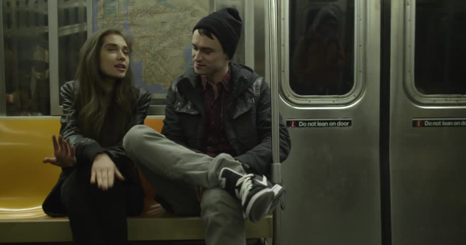A man and a woman sit next to each other and talk on a subway train