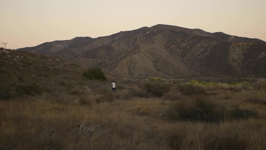 A person runs in the grass near a mountain at dusk