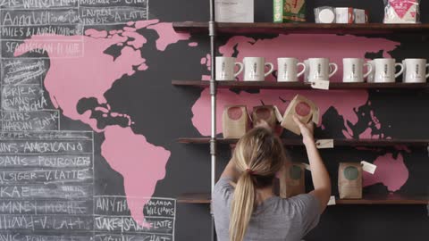 A woman places bags of coffee on a shelf in a coffee shop