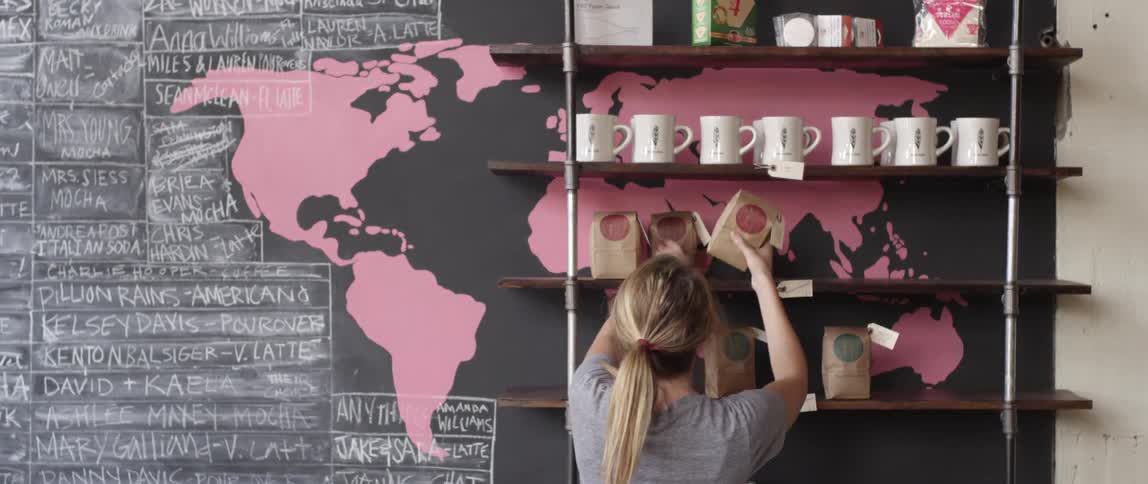 A woman places bags of coffee on a shelf in a coffee shop
