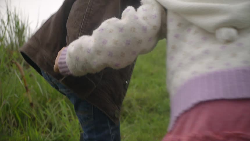 A boy and girl hold hands while they walk through a grassy area