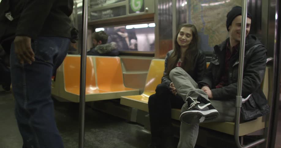 A man and woman sitting on a parked subway train and chatting as people depart
