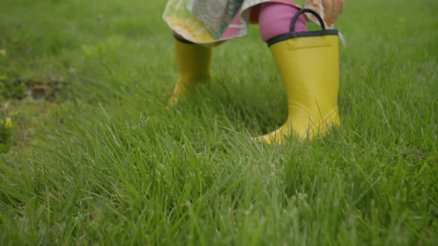 A toddler wears yellow rain boots in the grass