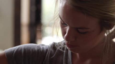 A blonde woman looking down at something and then picking up an unfolded coffee cup sleeve