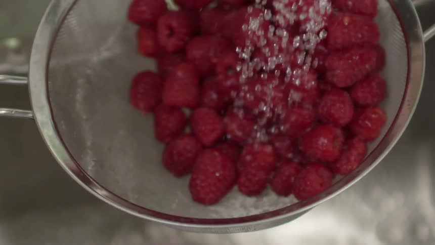 Raspberries being washed in a metal colander