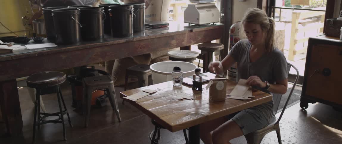 A woman sits at a table and stamps paper bags