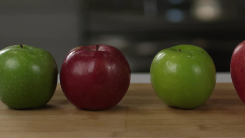 Five red and green apples lined up on a counter, then someone replaces one of the green ones with another green apple