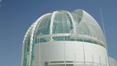 A large building with glass walls and a dome in front of a bright blue sky