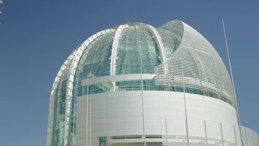 A large building with glass walls and a dome in front of a bright blue sky