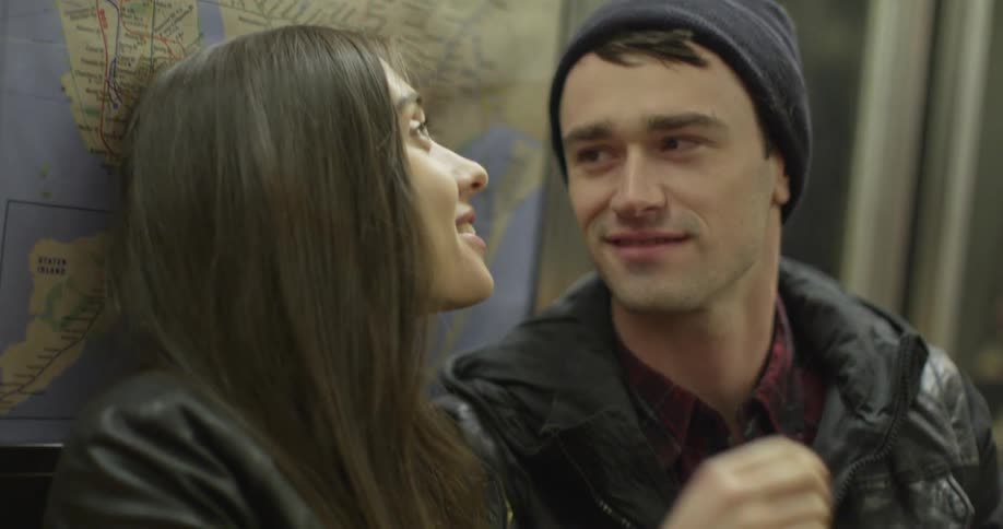 A man and a woman sit and talk in a train in front of a map