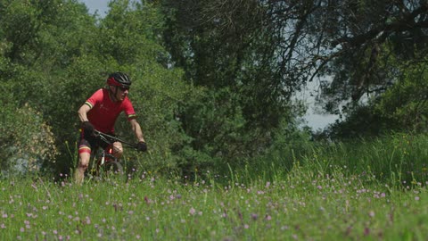A man rides a mountain bike through a green meadow full of tiny, purple flowers