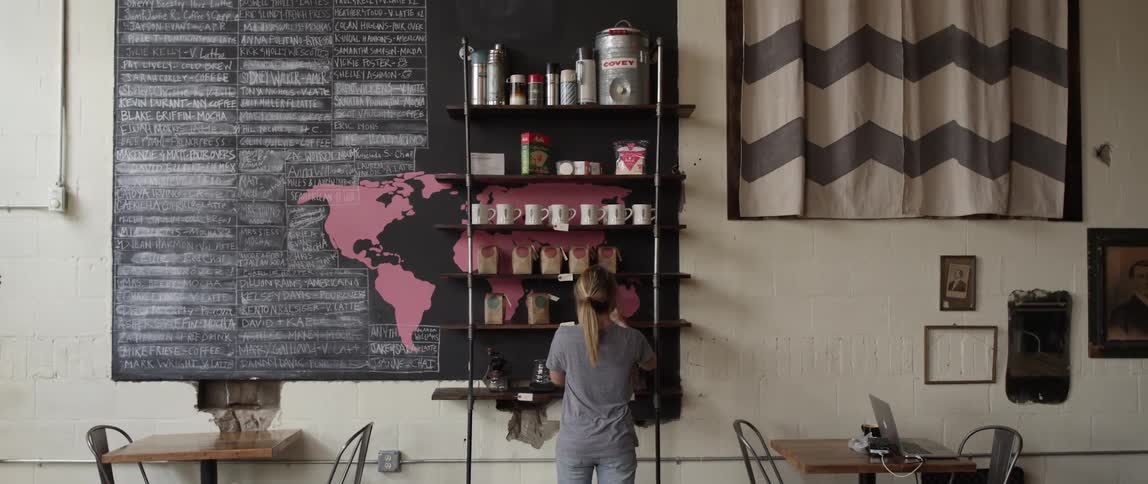 A woman places coffee on a shelf in a coffee shop